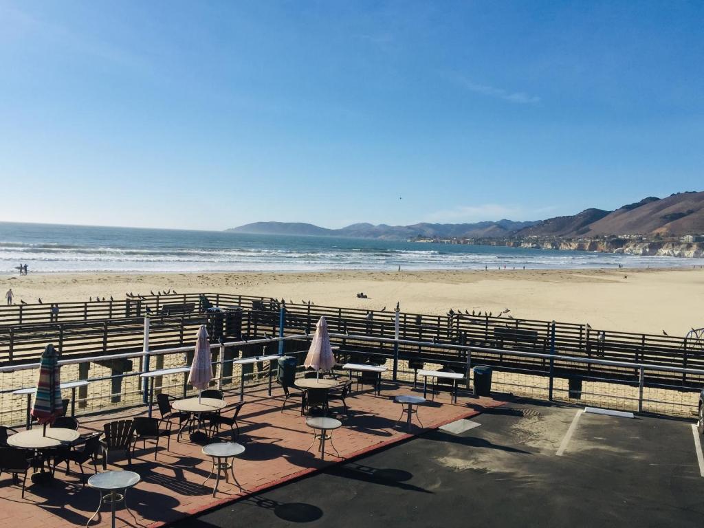 a beach with tables and umbrellas and the ocean at Dolphin Cove Motel in Pismo Beach