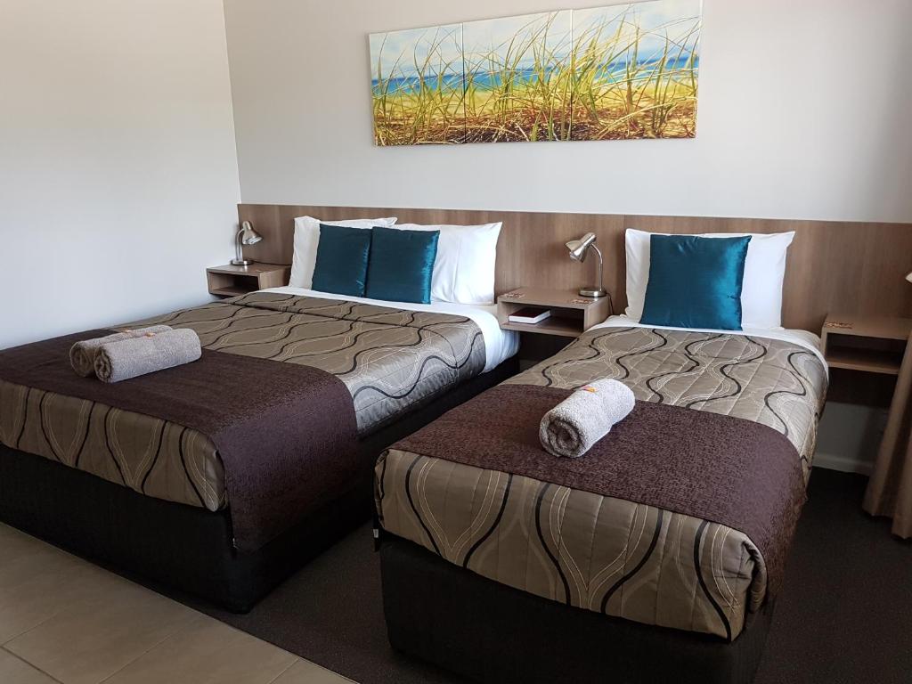 two beds in a hotel room with towels on them at Main Street Motel in Hervey Bay