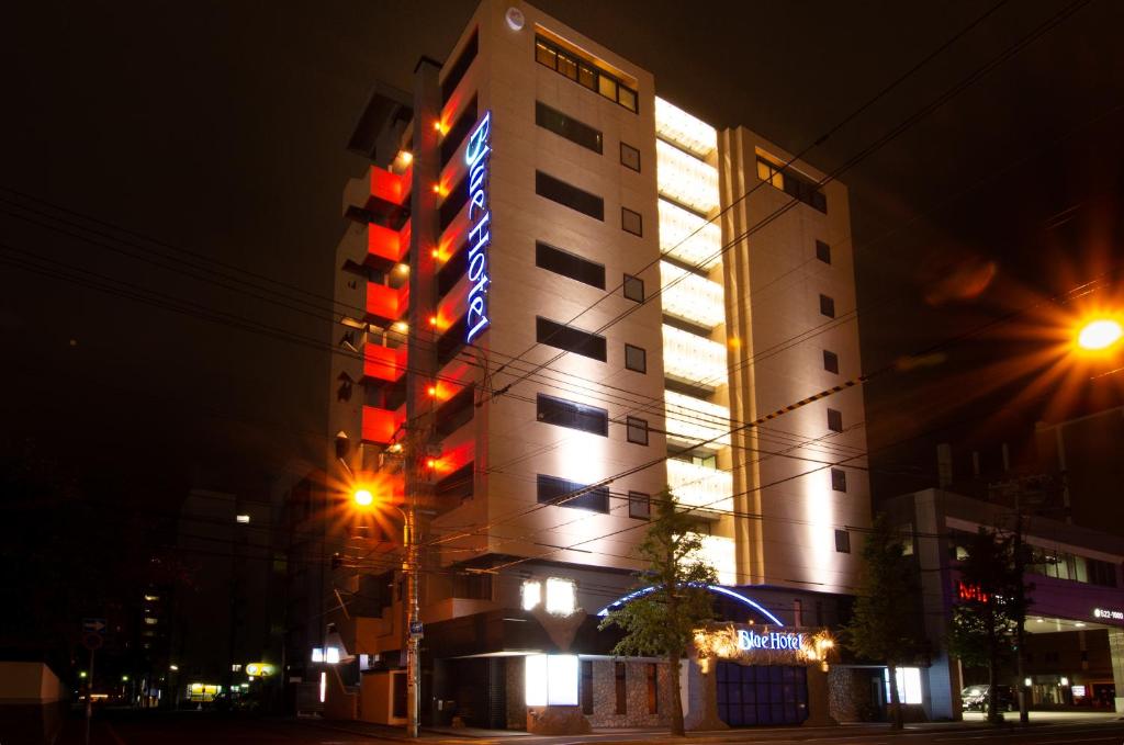 een hoog gebouw met 's nachts een bord bij BlueHotel sju(:)pri:m (Adult Only) in Sapporo
