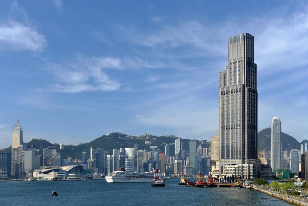 een skyline van de stad met een hoog gebouw en boten in het water bij Rosewood Hong Kong in Hong Kong