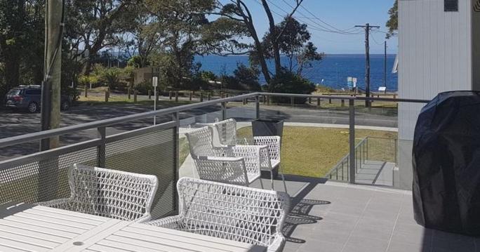 una fila de bancos blancos sentados en un balcón con vistas al océano en Beachfront Boogaloo, en Huskisson