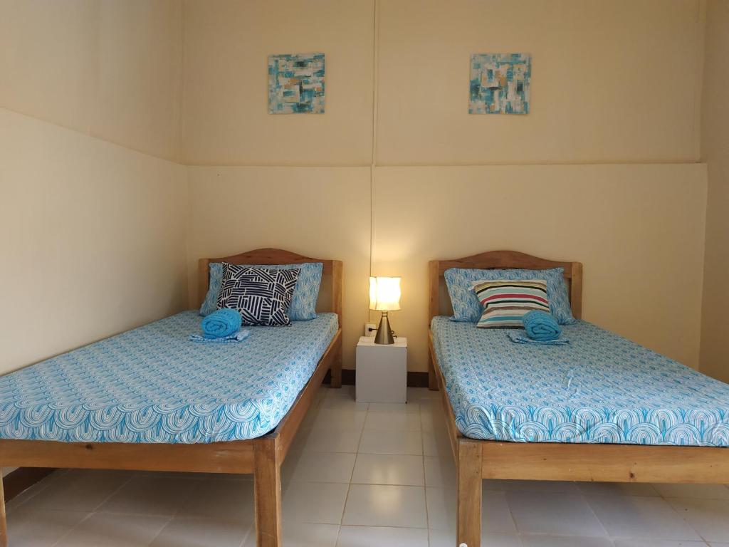two twin beds in a room with a lamp at Nelmann's Nipa Huts in San Vicente