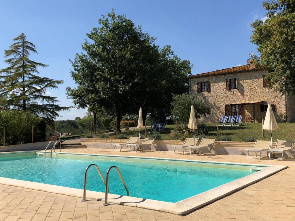 a swimming pool with chairs and umbrellas in front of a building at Agriturismo Podere Campinovi in Colle Val D'Elsa