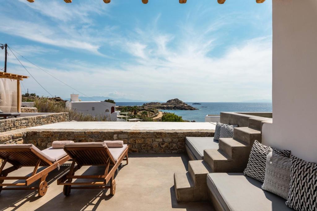 a patio area with chairs, tables and umbrellas at Trinity Mykonos - Villa & Beachfront Boutique Hotel in Platis Gialos