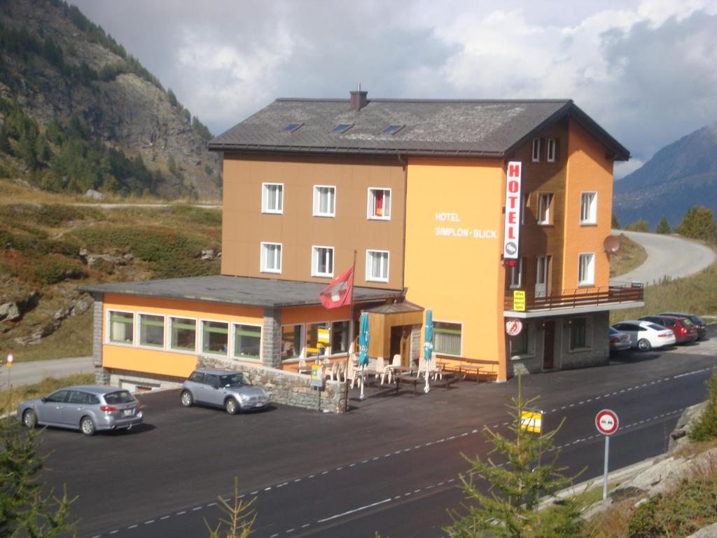 a large yellow building with cars parked in a parking lot at Hotel Simplon-Blick in Simplon Hospiz