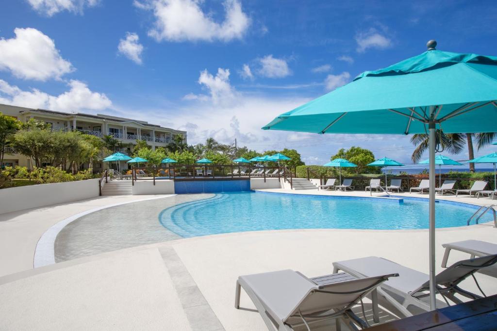 a swimming pool with chairs and a blue umbrella at Beach View Hotel in Saint James