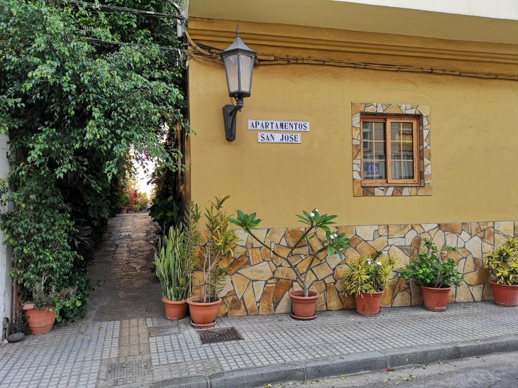 een bord aan de zijkant van een gebouw met potplanten bij Apartamentos San Jose in Valle Gran Rey