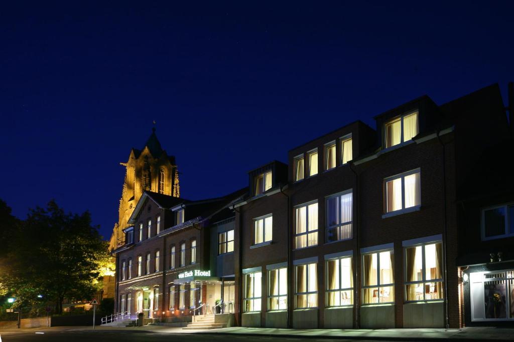 un gran edificio con una torre de reloj por la noche en Hotel von Euch, en Meppen