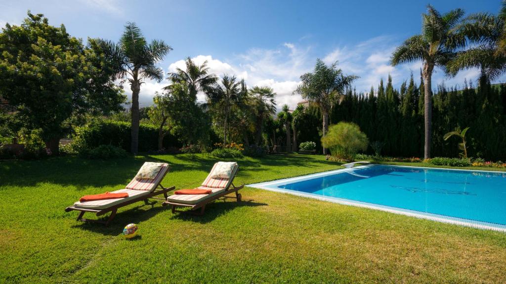 2 chaises assises dans l'herbe à côté d'une piscine dans l'établissement Lujoso apartamento en Finca Robles 2, à La Orotava