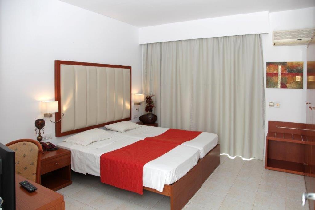a bedroom with a bed with a red and white blanket at Rodos Star Hotel in Afantou