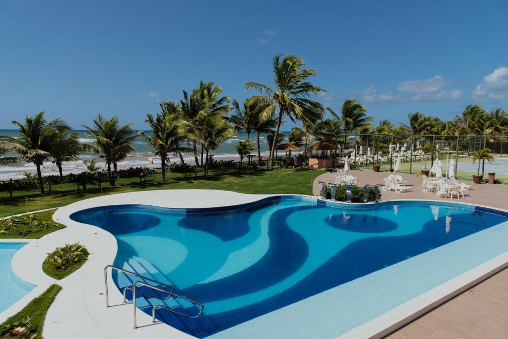 een zwembad in een resort met palmbomen en een strand bij Flat Guarajuba Beira da Praia pé na areia in Guarajuba