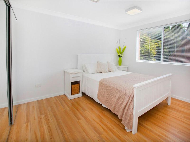 a white bedroom with a bed and a window at Waves Appartment in Kiama