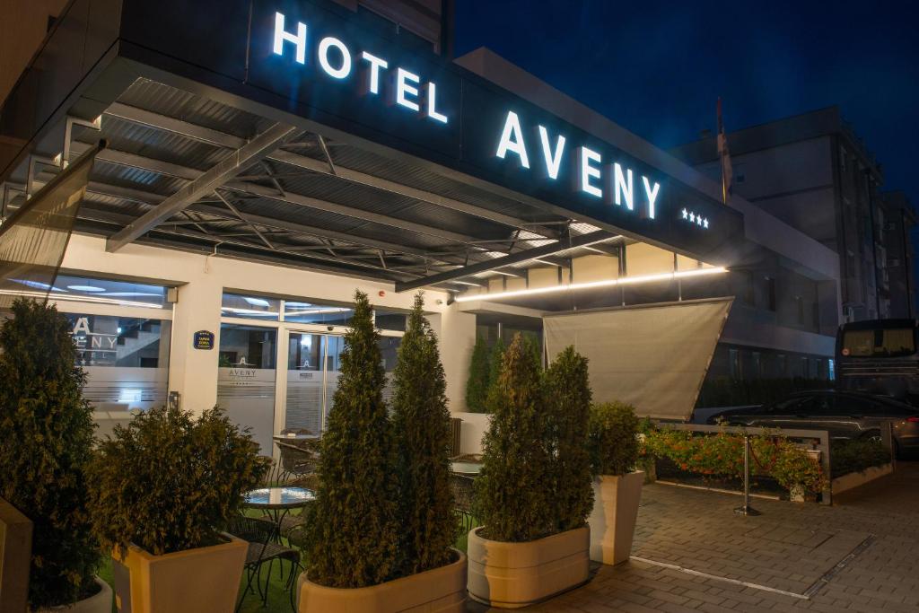 a hotelagency sign with potted trees in front of a building at Garni Hotel Aveny in Čačak