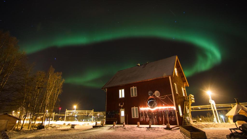 een huis met het noorderlicht in de lucht bij Abisko net Hostel & Huskies in Abisko