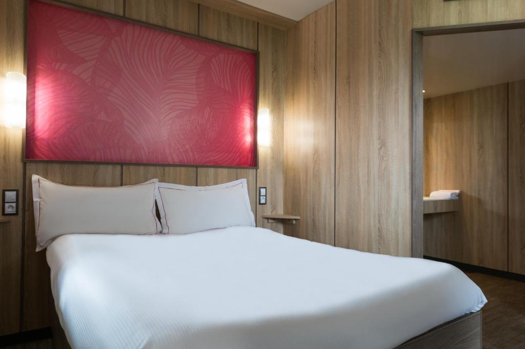 a large white bed in a room with a red wall at The Originals Access Aéroport, Hôtel Aurillac in Aurillac