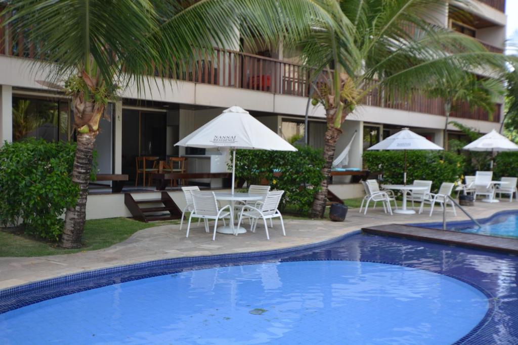 a resort pool with chairs and tables and palm trees at Nannai Residence in Porto De Galinhas