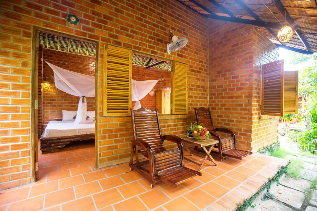 um pátio com cadeiras e uma cama num edifício de tijolos em Mekong Rustic Cai Be em Cái Bè