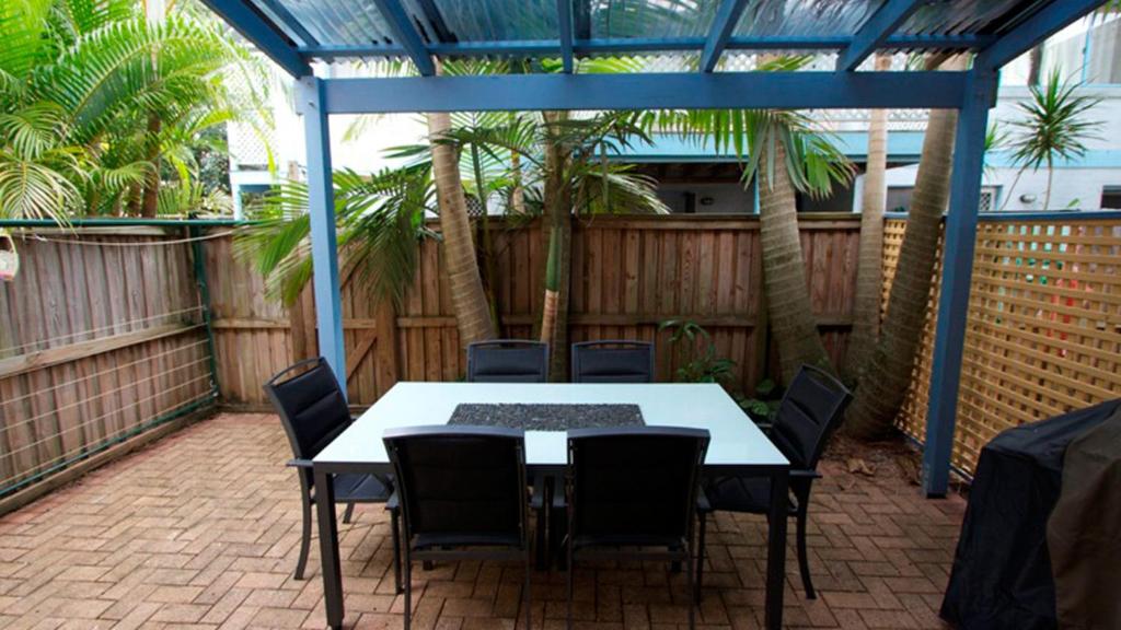 a table and chairs on a patio with palm trees at Byron Bay Accom Unit 3 41 Childe Street - Belongil Beach Apartment in Byron Bay