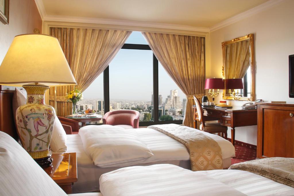 a hotel room with four beds and a desk and a window at Regency Palace Amman in Amman