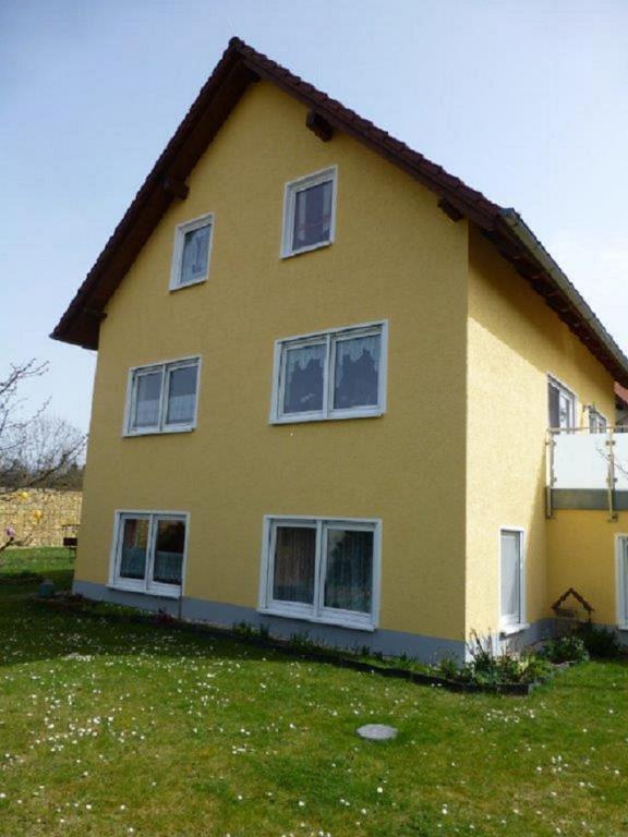 a yellow house with white windows on a grass field at Ferienwohnung Junghans in Saalfeld