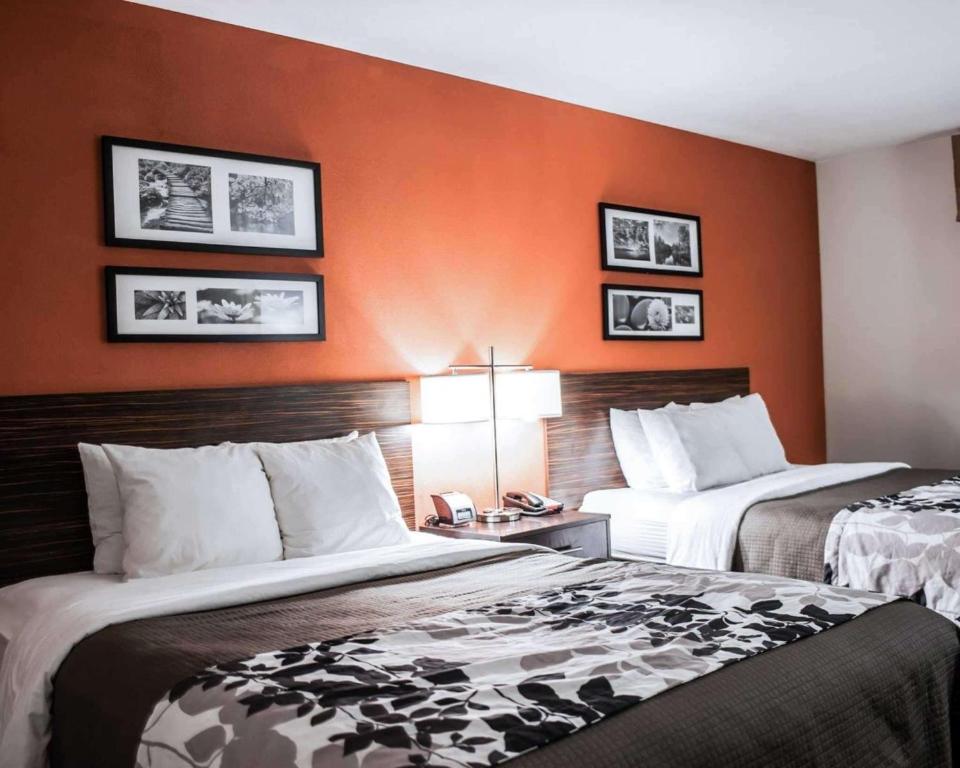 2 Betten in einem Hotelzimmer mit orangefarbenen Wänden in der Unterkunft Sleep Inn & Suites Fort Campbell in Oak Grove