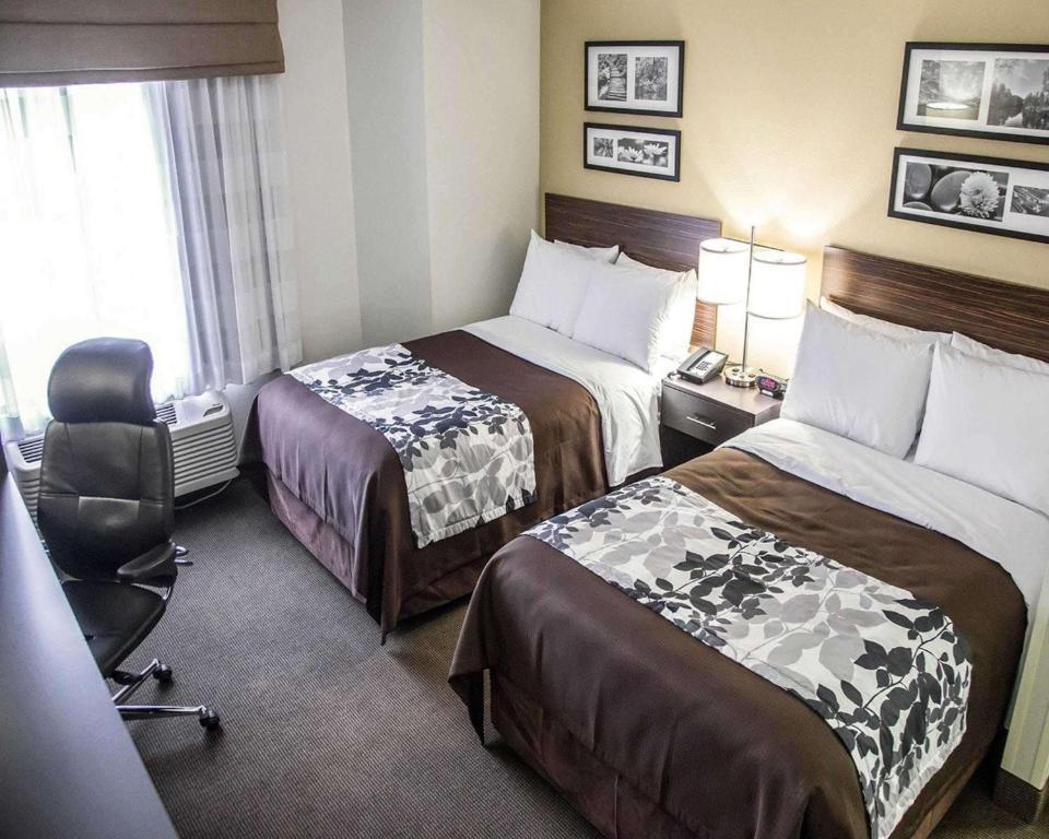 a hotel room with two beds and a chair at Sleep Inn Tinley Park I-80 near Amphitheatre-Convention Center in Tinley Park