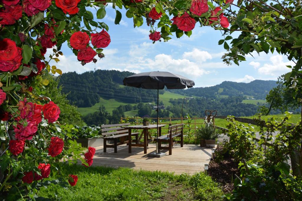 un tavolo di legno e panche con un ombrellone e delle rose di Bauernhof Schneider a Egg