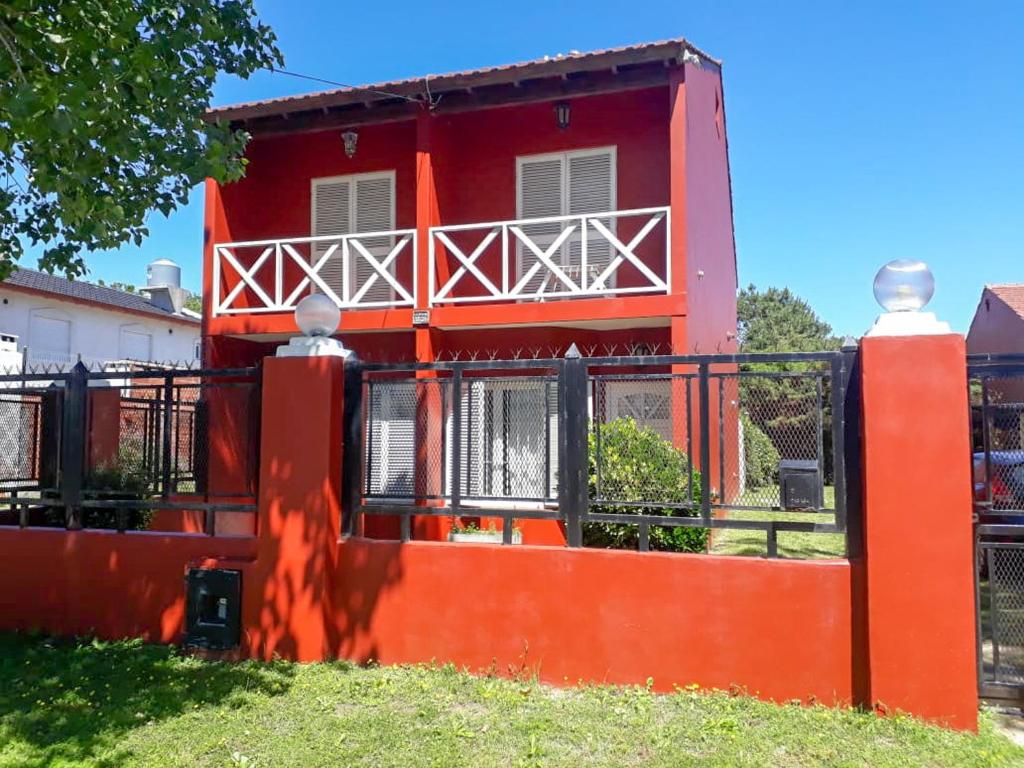 ein rotes Haus mit einem Zaun davor in der Unterkunft Complejo Mares in San Bernardo