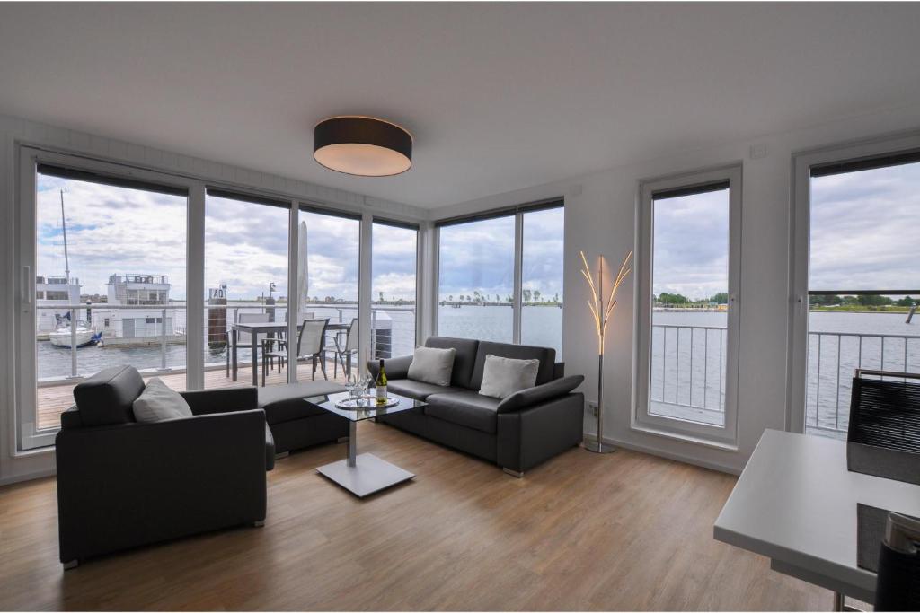 a living room with couches and a table and windows at Schwimmendes Haus Haithabu in Olpenitz