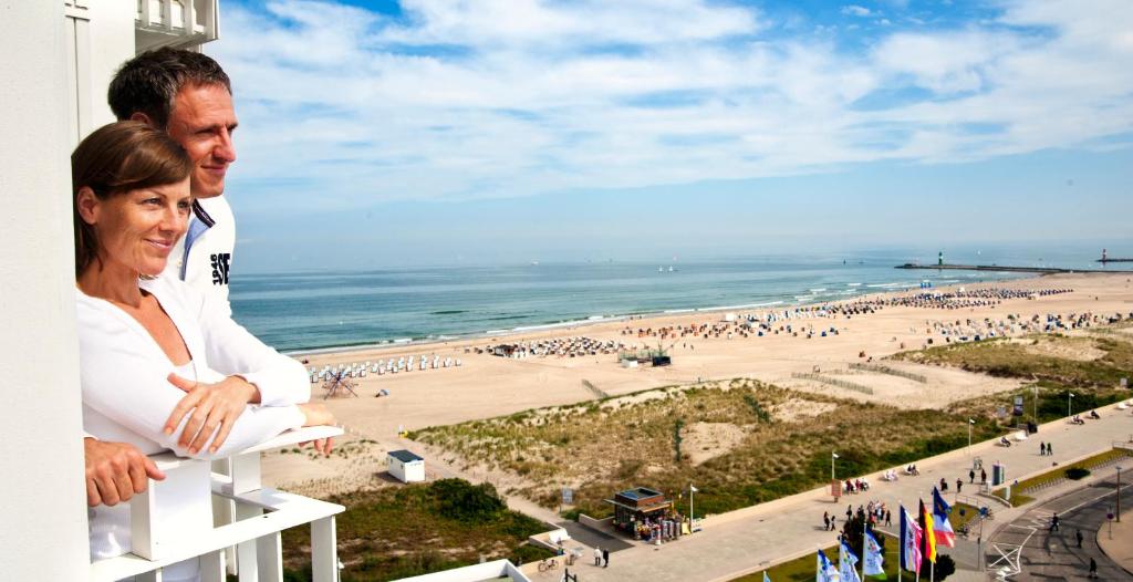 a man and a woman standing on a balcony overlooking a beach at Hotel Neptun in Warnemünde