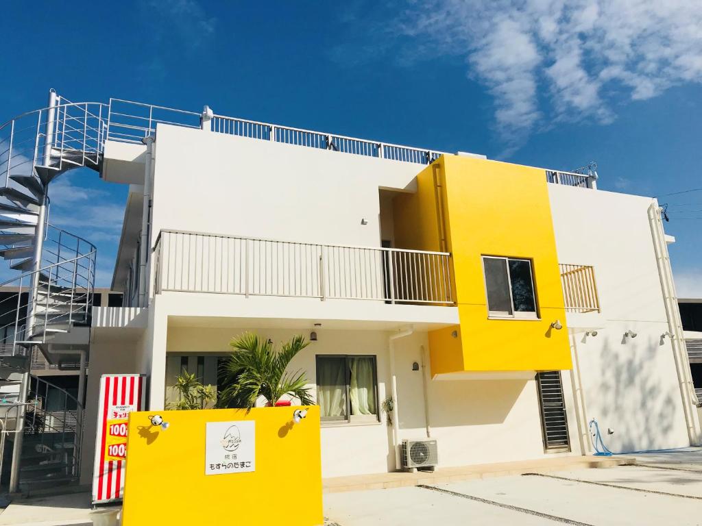 a white and yellow house with a yellow door at Hostel Mosura no Tamago in Motobu