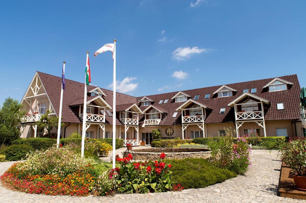un gran edificio con banderas y flores delante de él en Orchidea Hotel Lipót, en Lipót