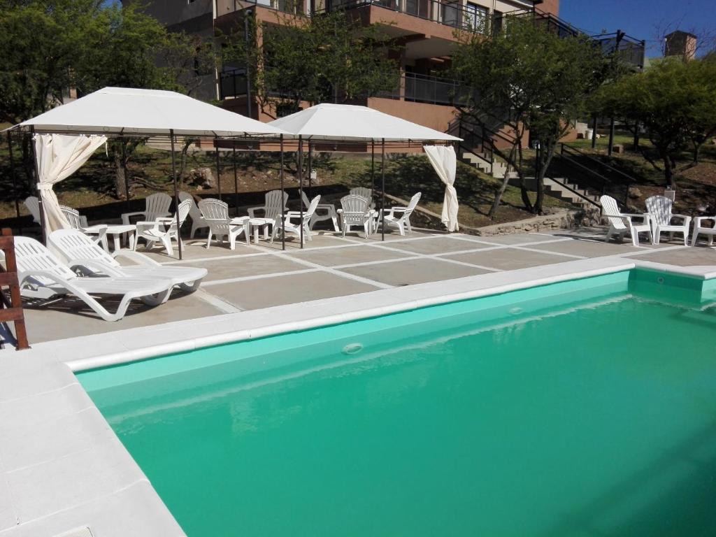 una piscina con sillas blancas, sombrillas y sillas en Cabañas El Mirador en Embalse