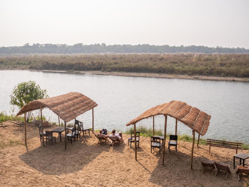a group of people sitting under umbrellas next to a river at Jungle Wildlife Camp in Sauraha