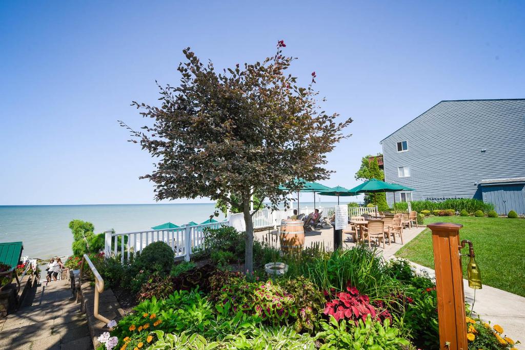 a garden with tables and a tree and the ocean at The Lakehouse Inn Geneva in Geneva-on-the-Lake