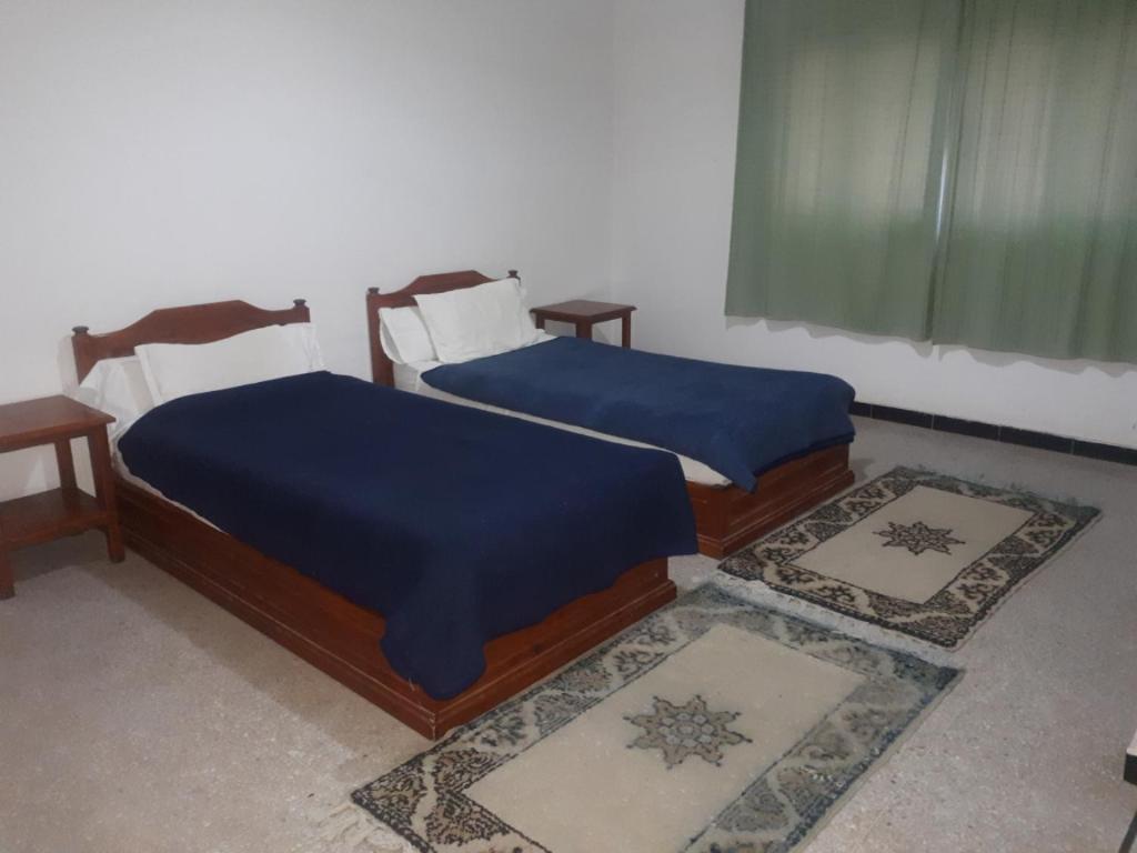 2 Betten mit blauen Decken in einem Zimmer mit Teppichen in der Unterkunft RESIDENCE OUARZAZATE in Ouarzazate