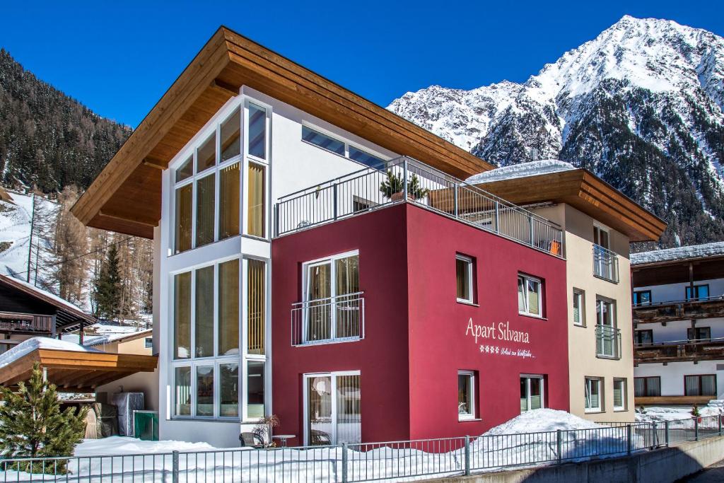 un edificio rojo con montañas en el fondo en Apart Silvana, en Längenfeld