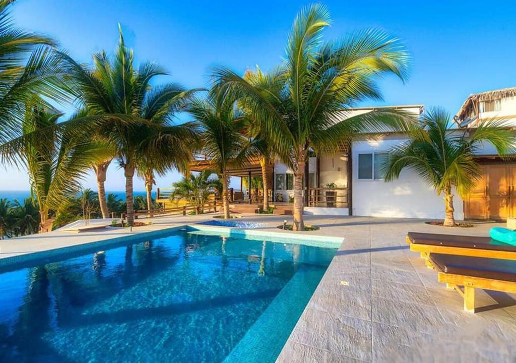 a swimming pool with palm trees in front of a house at Mar de Mancora Playa Las Pocitas in Máncora