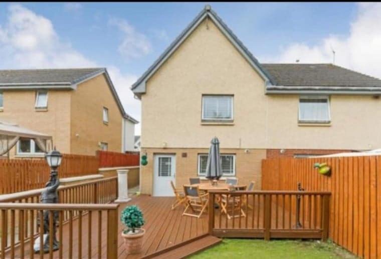 uma casa com um deque de madeira com uma mesa e cadeiras em Silverburn new house with free parking and nice garden em Glasgow