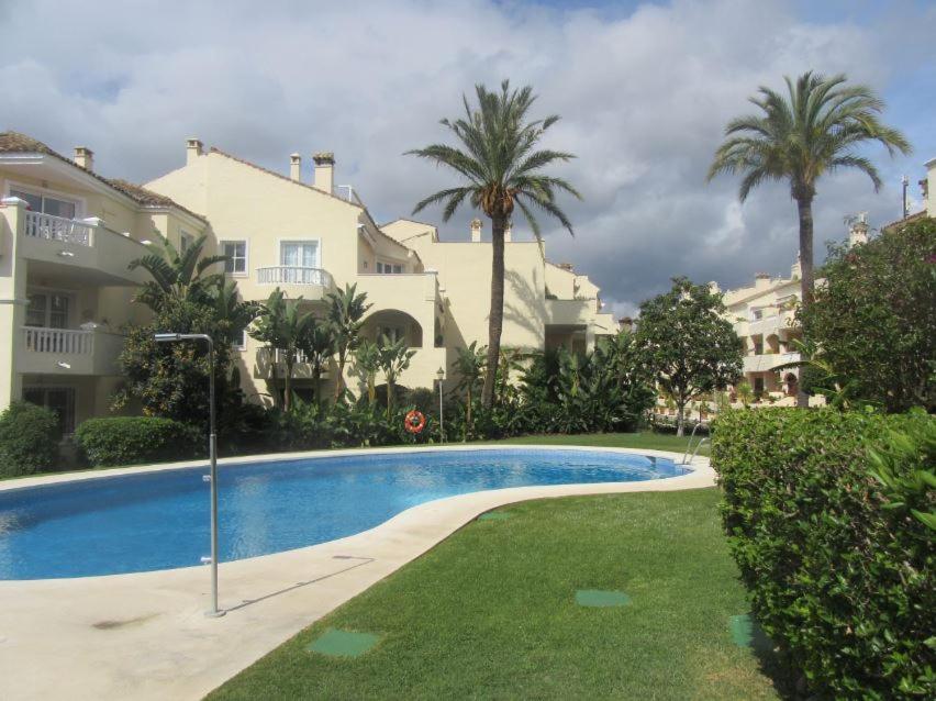 a swimming pool in front of a building with palm trees at Apartment near Puerto Banus in Estepona