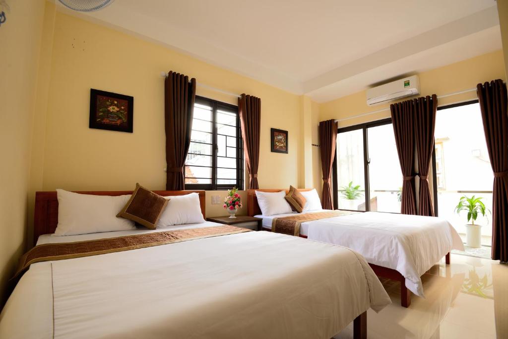two beds in a hotel room with windows at Guest House Maika in Hue