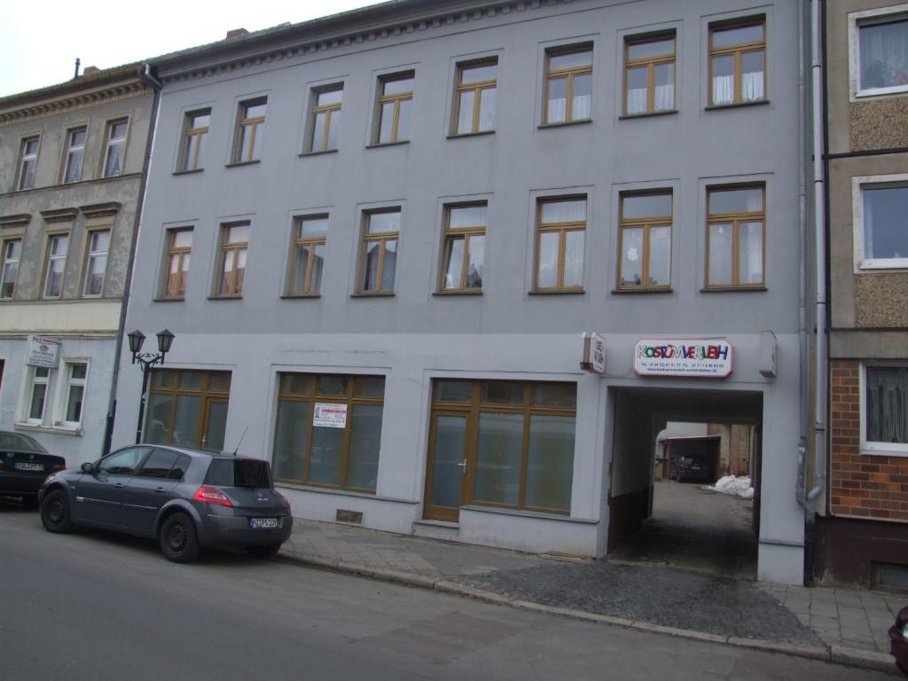 Un bâtiment blanc avec une voiture garée devant. dans l'établissement Hostel Vorharz Aschersleben, à Aschersleben