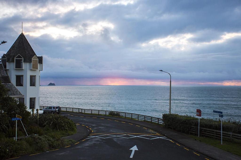 a house on a road next to the ocean at DOLLY KIWI ICONIC BACH IN PRIME LOCATION in New Plymouth