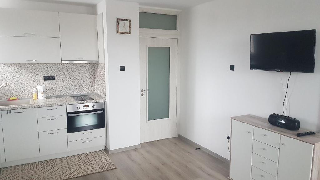 a kitchen with white cabinets and a tv on the wall at Roza Apartment in Varna City