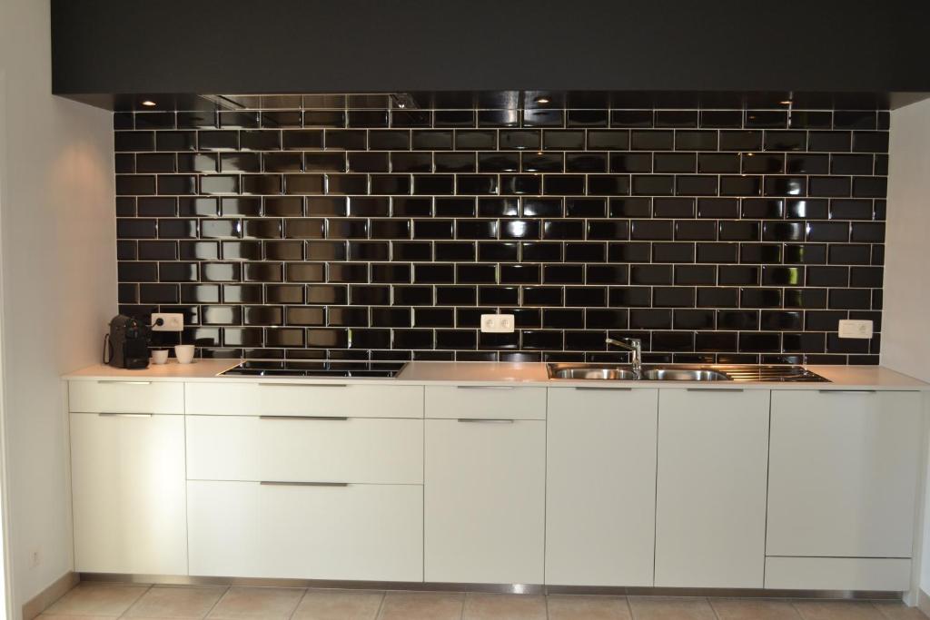 a kitchen with white cabinets and a black tile wall at Vue d'en Haut in Durbuy