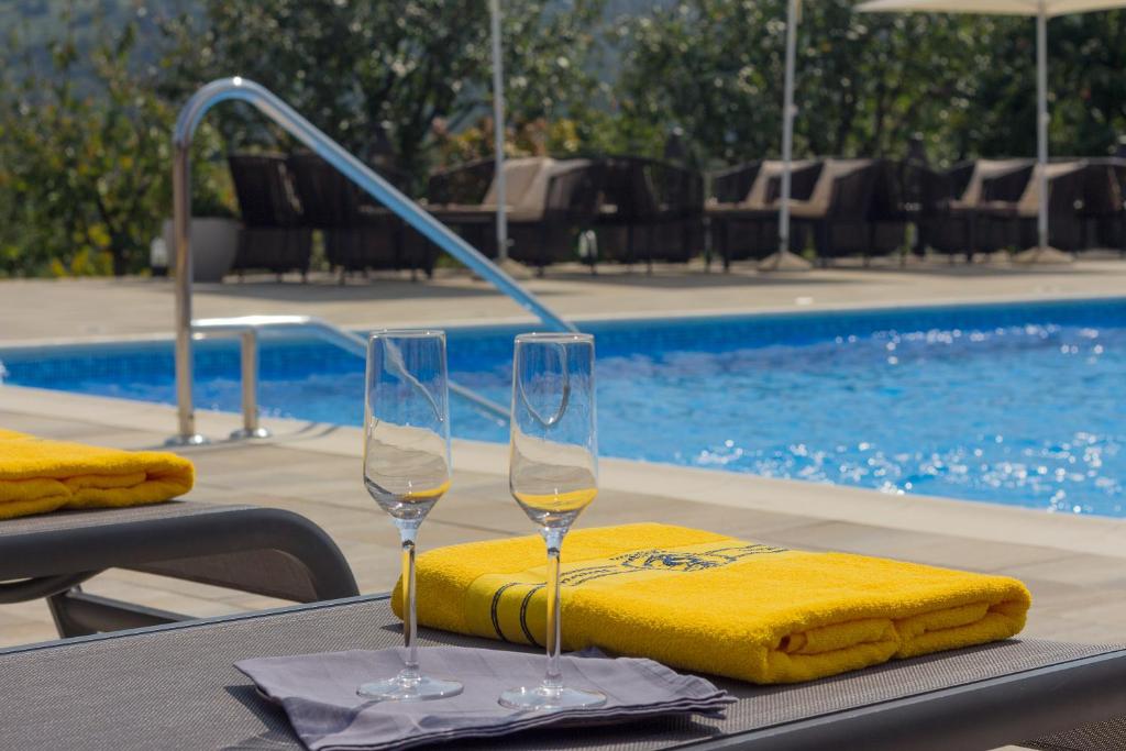 two wine glasses sitting on a table next to a pool at Hotel Degenija in Seliste Dreznicko