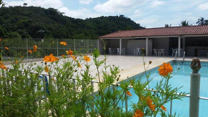 a house with a swimming pool with flowers in the foreground at Sitio cachoeira de macacu in Guapimirim
