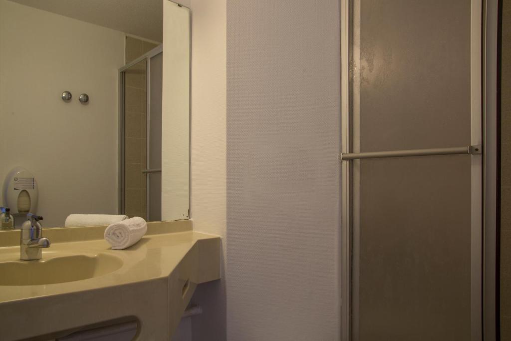 a bathroom with a sink and a shower with a mirror at The Originals City, Hôtel Amys, Tarbes Sud (Inter-Hotel) in Odos
