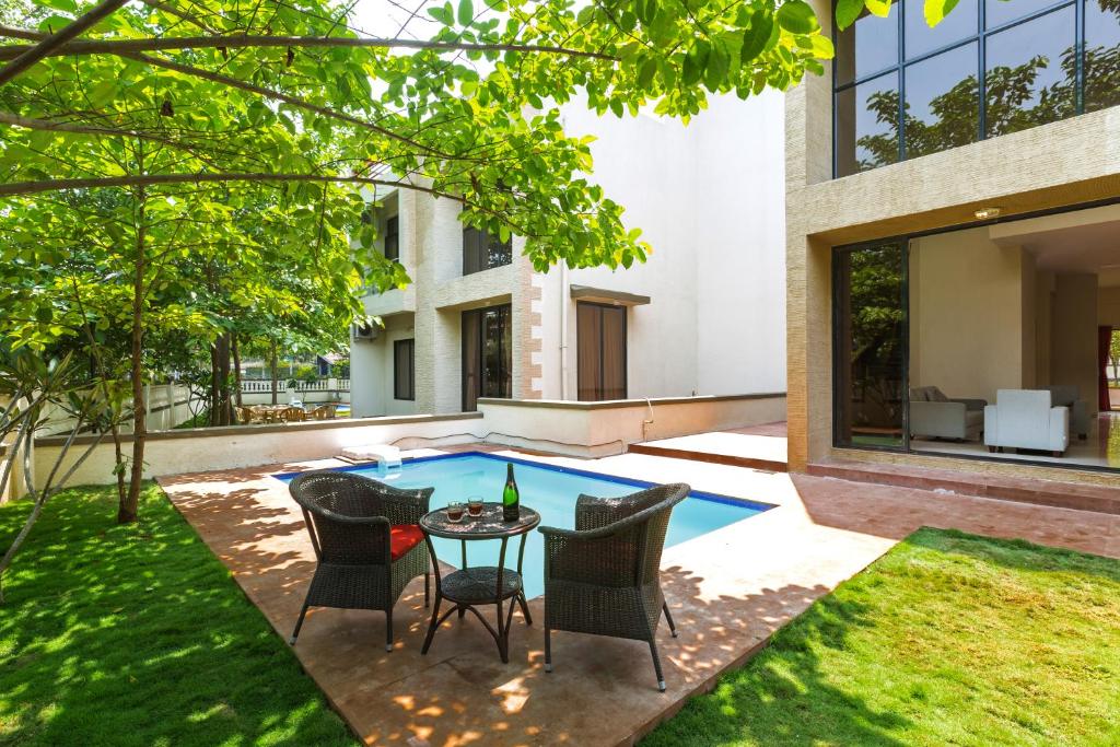 une terrasse avec une table, des chaises et une piscine dans l'établissement StayVista's Greenwoods Villa 6 - City-Center Villa with Private Pool, Terrace, Lift & Ping-Pong Table, à Lonavala