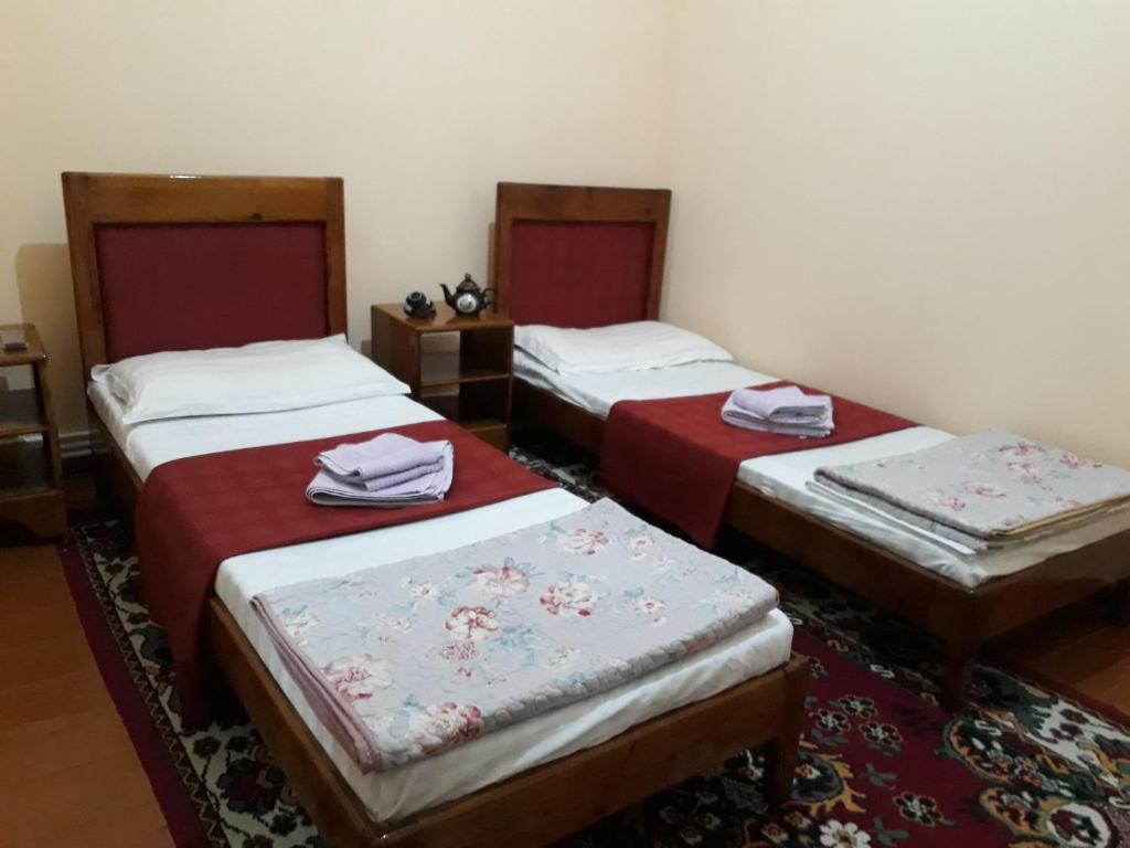 drie bedden in een kamer met rode lakens bij Amir-Yaxyo Hotel in Bukhara
